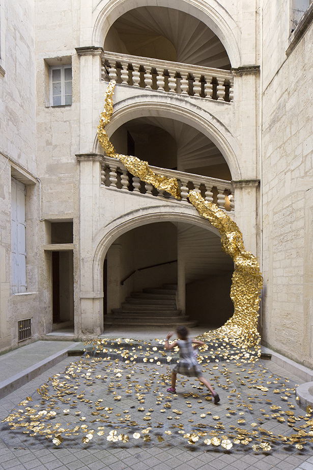 A ribbon of gold artificial flowers cascades through three stone arches into a courtyard while a child runs across the foreground